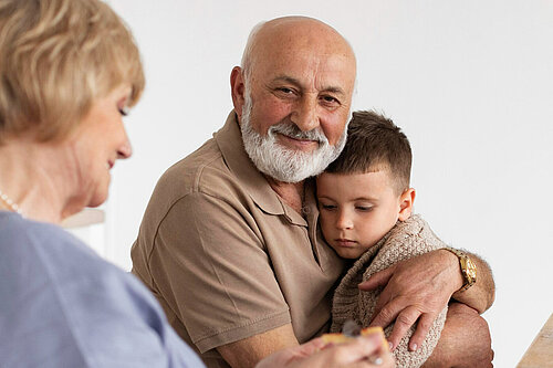 An older man hugs a young child, sat next to him is an older woman